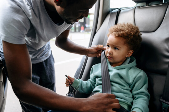Smiling father adjusting seat belt of daughter in car