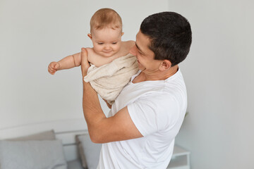 Portrait of handsome optimistic young adult father with his toddler baby girl, looking at kid...