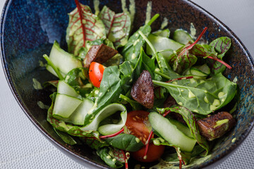 vegetable salad with meat, cherry tomatoes, cucumbers and herbs in a blue plate on a gray background close-up