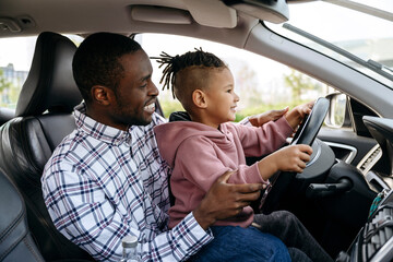 Smiling father and son playing with steering wheel in car