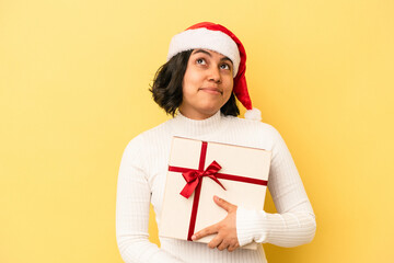 Young latin woman celebrating christmas holding a gift isolated on yellow background dreaming of achieving goals and purposes