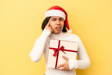 Young latin woman celebrating christmas holding a gift isolated on yellow background showing a disappointment gesture with forefinger.