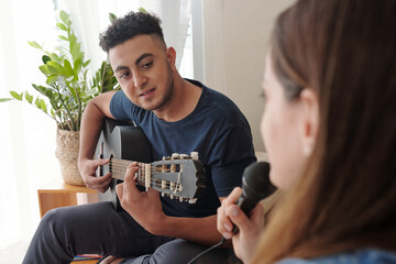 Man playing acoustic guitar and looking at pretty wife or girlfriend singing song in microphone