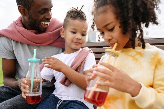 Father looking at children drinking lemonade in park