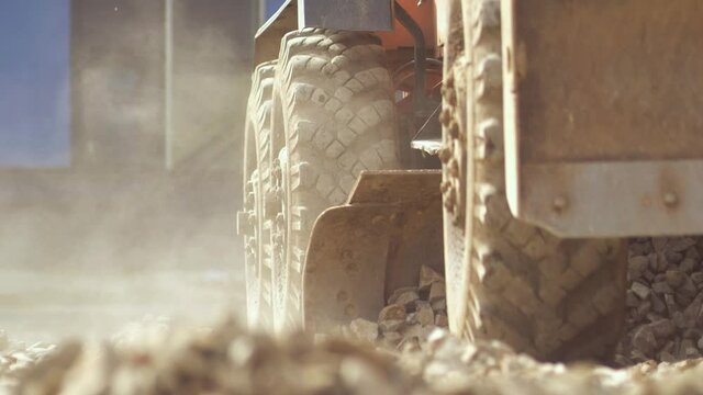 Tractor moves towards the camera, raises a cloud of dust, raking up a pile of stones with the excavator bucket. Close up view. Preparation of the surface for asphalt paving