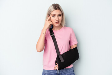 Young caucasian woman with broken hand isolated on blue background showing a disappointment gesture with forefinger.