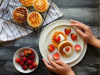 The girl's hand decorates freshly prepared cheesecakes with fresh red strawberries