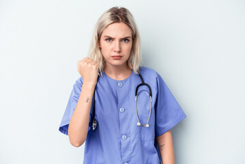 Young nurse woman isolated on blue background showing fist to camera, aggressive facial expression.