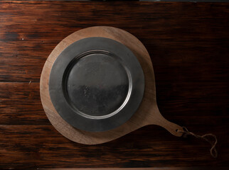 Mesa con tabla y plato redondo negro vacío, vista cenital. Table with table and empty black round plate, overhead view.