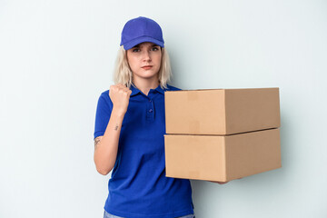 Young delivery caucasian woman isolated on blue background showing fist to camera, aggressive facial expression.