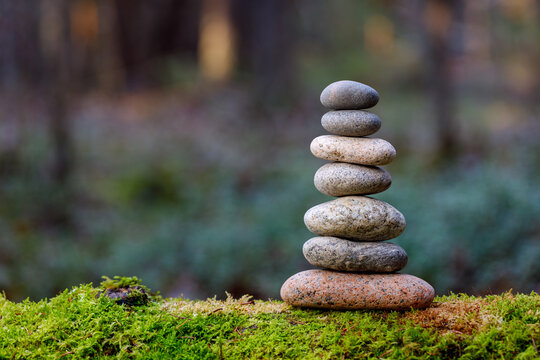 Pyramid stones balance on old mossy fallen tree. Stone pyramid in focus. Forest background blurred
