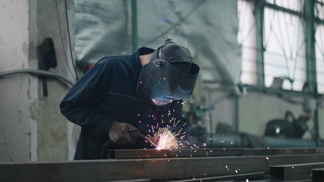 A working welder in a protective mask connects metal parts with gas or electric welding in slow motion