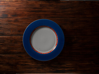 Plato redondo azul vac&iacute;o sobre tabla de madera. Vista cenital. Round empty blue plate on wooden board. Zenithal view.