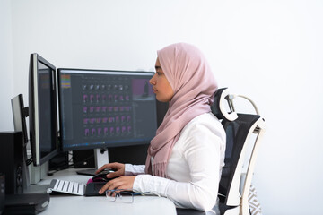 Female Arabic creative professional working at home office on desktop computer with dual screen monitor top view. Selectve focus 