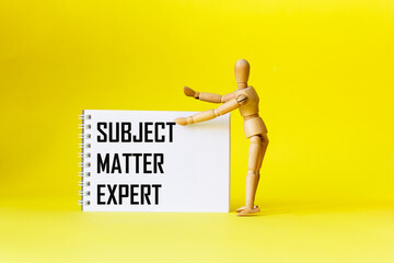 A notebook with the text EXPERT MATTER SUBJECT on a yellow background with a wooden doll. 