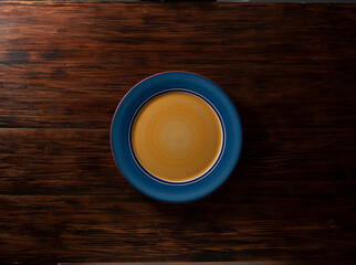 Plato redondo azul y amarillo vacío sobre tabla de madera. Vista cenital. Round empty blue and yellow  plate on wooden board. Zenithal view.