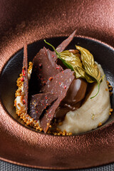 chocolate mousse with whipped cream, decorated with leaves covered with food-grade gold close-up on a bronze plate