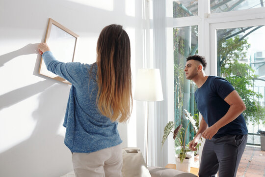 Woman asking boyfriend to check if she is hanging the picture frame evenly
