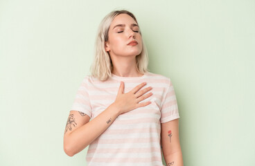 Young caucasian woman isolated on green background taking an oath, putting hand on chest.