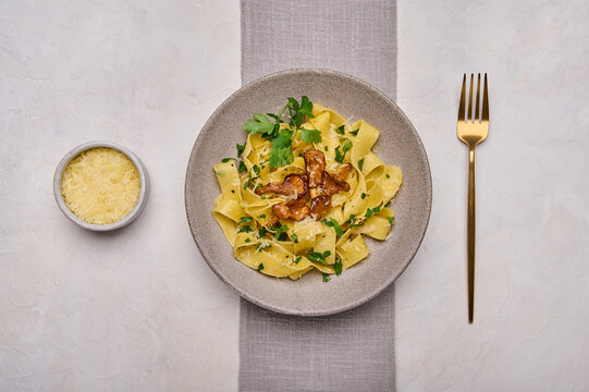 Flat lay traditional pasta pappardelle with mushrooms chanterelles, cheese and parsley on plate with golden fork and napkin