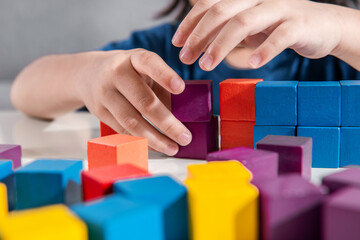Close-up of young little toddler girl hand plays with wooden colorful toy block at home or preschool. Toy Blocks for Education Development Construction and creative toys Concept Idea. Selective focus