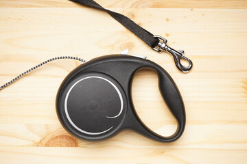 Black retractable leash for dogs on a wooden background, close-up. Flat lay.