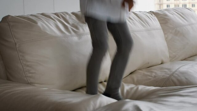 Legs of active child jumping on couch at home, closeup shot