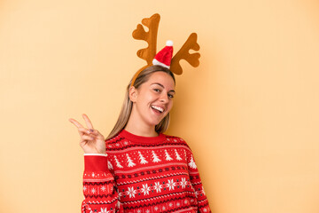 Young caucasian woman wearing a christmas reindeer hat isolated on yellow background joyful and carefree showing a peace symbol with fingers.