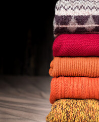 On the bed is a stack of orange-colored wool sweaters. Copy space. Vertically.