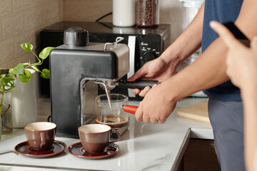 Fototapeta na wymiar Hands of man using coffee machine when making coffee for himself and girlfriend