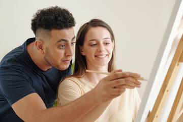 Fototapeta premium Creative young man painting on canvas with hand of his girlfriend