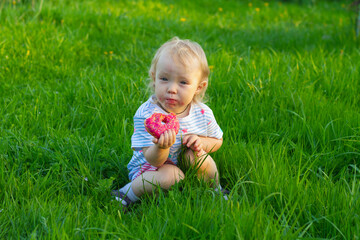 Baby girl is resting on the lawn on a hot summer day and eating a sweet donut