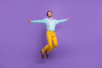 Full size photo of joyful millennial guy jump wear tie suspenders shirt pants footwear isolated on purple background