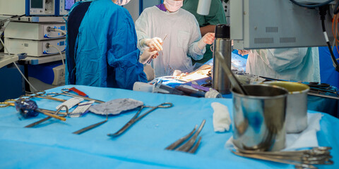 Sterilized surgical instruments on a blue table in the operating room. Selective focus. In the background, surgeons operate on a patient. Surgical equipment.