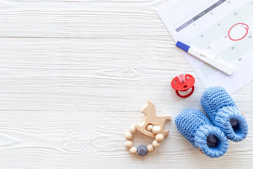 Blue baby boy booties with pregnancy test on calendar, top view