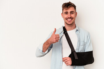 Young caucasian man with broken hand isolated on white background smiling and raising thumb up