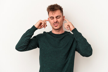 Young caucasian man isolated on white background covering ears with fingers, stressed and desperate by a loudly ambient.