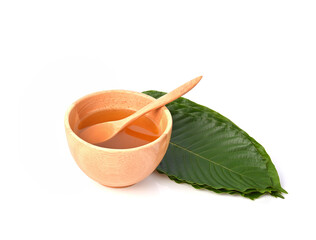 Mitragyna speciosa water in wooden spoon and bowl and leaves on white background.