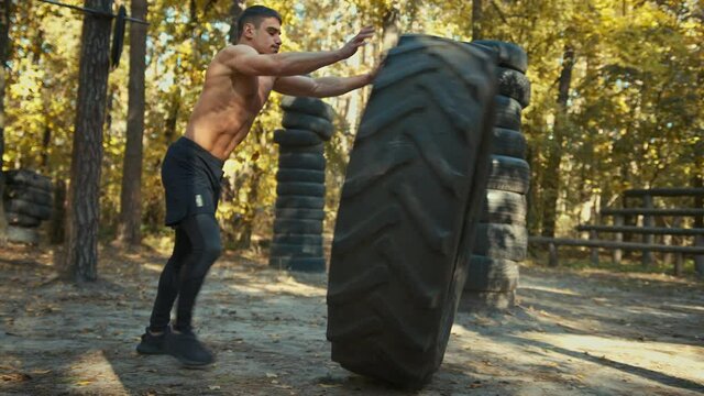 Man working out with a huge tire, turning and flipping in the forest gym. Strength and motivation