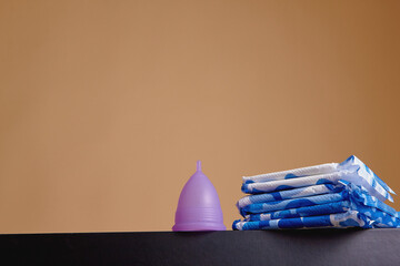 A silicone menstrual cup next to a stack of sanitary towels. Sustainability, zero waste, frugality concept. Alternative way to manage periods, menstrual cycles