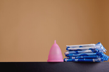 A silicone menstrual cup next to a stack of sanitary towels. Sustainability, zero waste, frugality...