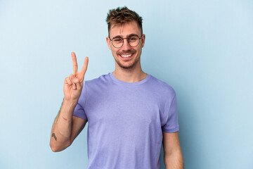 Young caucasian man isolated on blue background joyful and carefree showing a peace symbol with fingers.