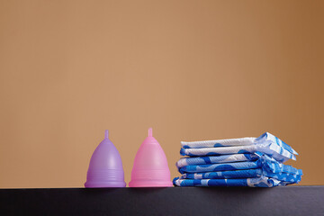 A silicone menstrual cup next to a stack of sanitary towels. Sustainability, zero waste, frugality concept. Alternative way to manage periods, menstrual cycles