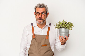 Middle age gardener caucasian man holding a plant isolated on white background  confused, feels...