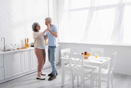 Smiling middle aged couple dancing in kitchen.