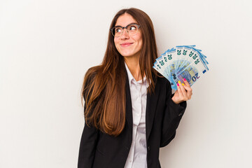 Young caucasian business woman holding banknotes isolated on white background dreaming of achieving goals and purposes