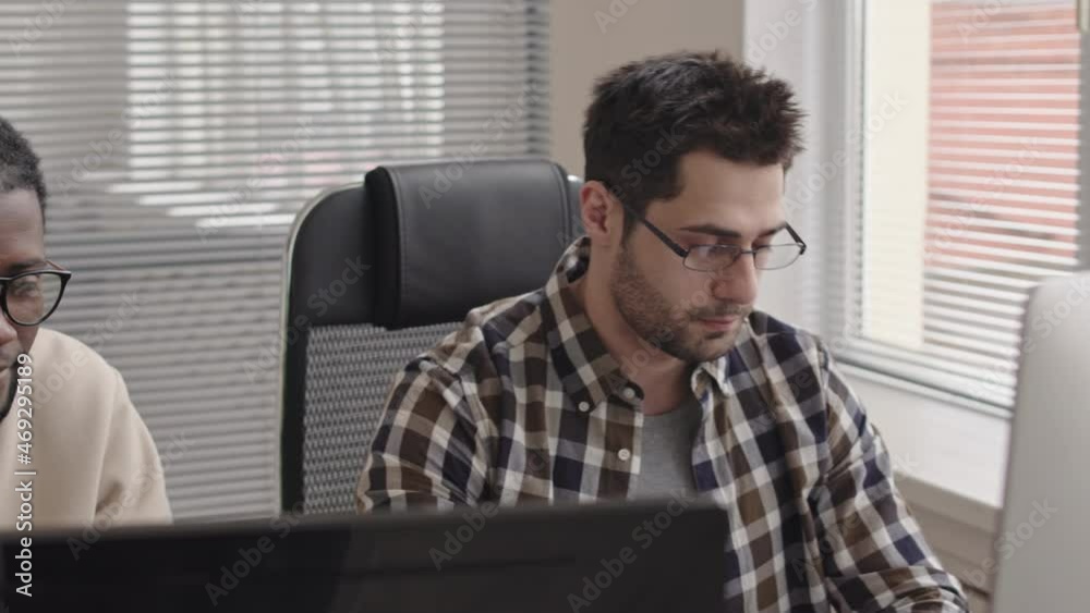Wall mural panning chest-up shot of two young multi-ethnic programmers sitting in front of computer monitors in