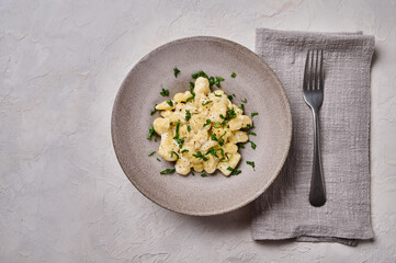 Gnocchi, prepared with potato and whole grain flour dough with cream sauce and parsley on gray concrete background with black fork and napkin. Top view. Copy space