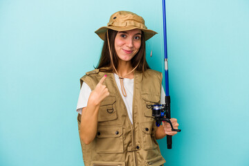 Young caucasian fisherwoman isolated on blue background pointing with finger at you as if inviting come closer.
