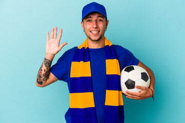 Young soccer fan man holding a ball isolated on blue background  smiling cheerful showing number...